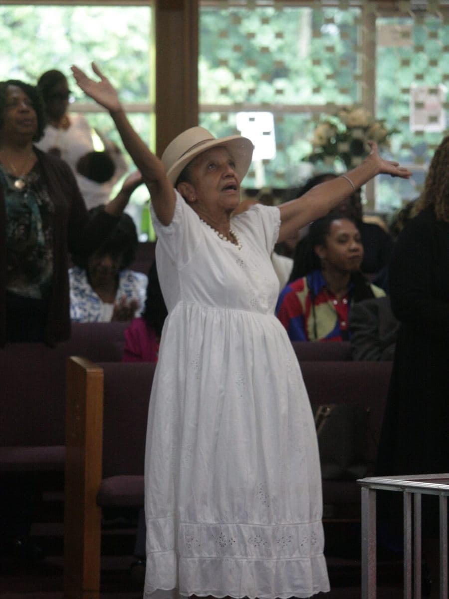 A member in white, arms raised in praise during worship